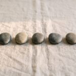 A neat row of seven smooth stones evenly spaced on soft linen, suggesting a steady, regular rhythm